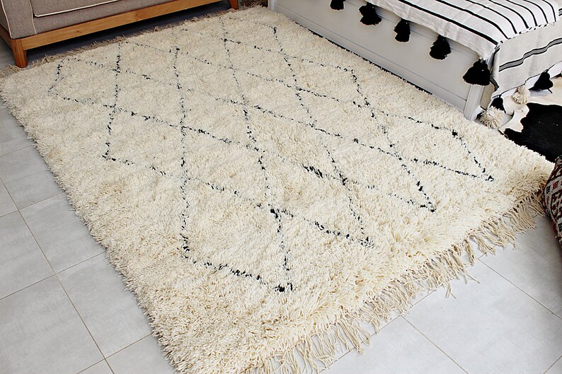 May include: A white shag rug with a black diamond pattern. The rug has fringe on all sides.