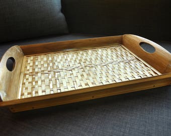 Può includere: Un vassoio rettangolare in legno con un inserto in bambù intrecciato. Il vassoio ha due maniglie sui lati.