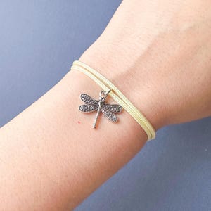 May include: A yellow cord bracelet with a silver dragonfly charm.