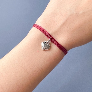 Op de afbeelding: Een rood koord armband met een zilveren aardbei bedel.