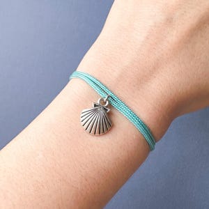 May include: A turquoise blue braided cord bracelet with a silver seashell charm.