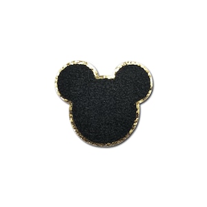 May include: A black patch in the shape of a mouse head with gold glitter trim. The patch has a textured appearance and is set against a white background. This patch is suitable for clothing or accessories.