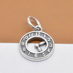 Op de afbeelding: Zilveren bedel in de vorm van een wijzerplaat met Romeinse cijfers en een kleine wijzer in het midden.