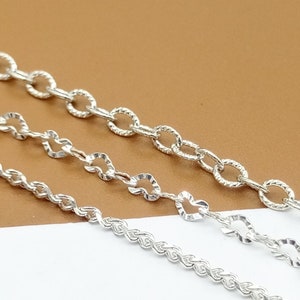 Könnte beinhalten: Drei silberne Ketten in verschiedenen Stilen und Stärken. Die Ketten liegen auf einer braunen und einer weißen Oberfläche.