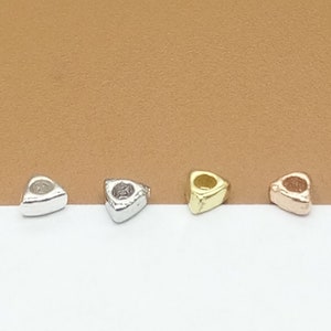 Könnte beinhalten: Vier dreieckige Metallperlen in Silber, Gold und Roségold.