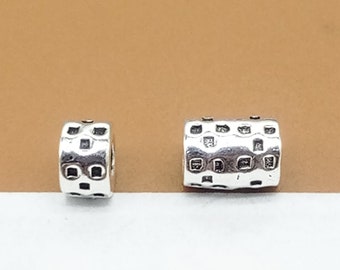 May include: Two silver spacer beads with a textured square pattern. The beads are cylindrical in shape.