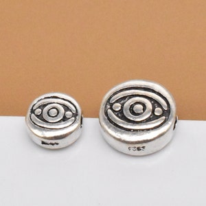 May include: Two silver-toned round beads with an eye design. The larger bead is about 1.5 cm in diameter and the smaller bead is about 1 cm in diameter.