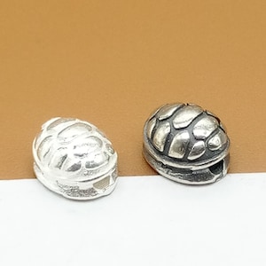 Peut inclure: Deux perles en argent en forme de tortue, l'une avec une finition polie et l'autre avec une finition texturée.