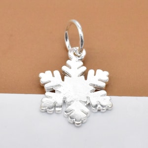 Op de afbeelding: Een zilveren sneeuwvlok-bedel met een springring om aan een armband of ketting te bevestigen.