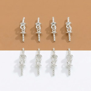 May include: Eight silver-colored jewelry findings are arranged in two rows. Each finding has a decorative top with a looped design, a central section, and a twisted, tapered post. The background is divided into brown and white sections.