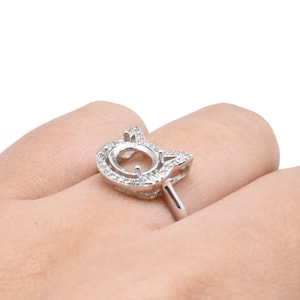 May include: A silver ring with a unique cat-shaped design. The ring features a central setting surrounded by small, sparkling stones. The ring's band is thin and polished, and the overall design is elegant and eye-catching.