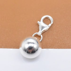 May include: A silver charm with a round ball and a lobster clasp.