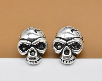 May include: A pair of silver skull stud earrings. The skulls have detailed features, including eye sockets, a nose, and a mouth.