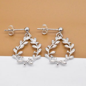 Puede incluir: Un par de pendientes de plata con un delicado diseño de hojas. Los pendientes están hechos de metal y tienen un estilo simple y elegante.