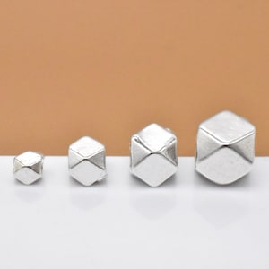 May include: Four silver geometric beads of varying sizes. The beads are all in the shape of a cube with rounded edges.