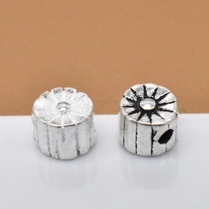 May include: Two silver metal beads with different designs. One bead has a circular design with a raised center, while the other bead has a starburst design with a raised center.