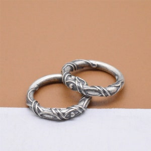 May include: Two silver rings with a twisted, textured design. The rings are intertwined and have a smooth, polished finish.