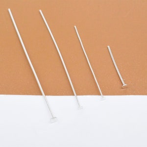 Könnte beinhalten: Vier silberfarbene Stiftstifte in verschiedenen Längen, jeweils mit einem flachen, runden Kopf. Die Stifte sind diagonal vor einem braunen und weißen Hintergrund angeordnet, geeignet für Schmuckherstellung oder Bastelprojekte.