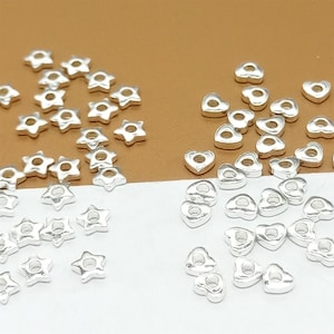 May include: A collection of silver-toned metal star and heart shaped beads. The beads have a hole in the center for stringing.