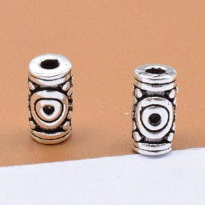 May include: Two silver metal beads with intricate designs. The beads are cylindrical and have a small hole in the center.
