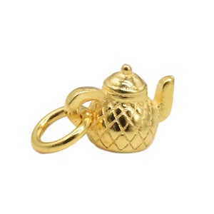 May include: A gold-colored teapot charm with a diamond pattern. The charm has a loop for attaching to a bracelet or necklace.
