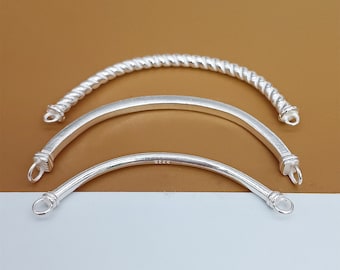 Puede incluir: Tres brazaletes en blanco de plata con diferentes estilos. El brazalete superior es un diseño de cuerda trenzada. El brazalete del medio es una forma de semicírculo liso y redondeado. El brazalete inferior es una forma de semicírculo liso y redondeado, más delgado.