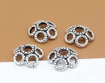 May include: Four silver-toned metal bead caps with a decorative, circular, rope-like design. Each cap has five circles.