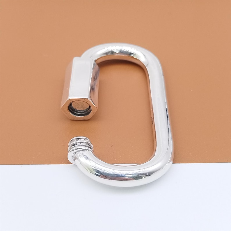 May include: A shiny, silver-colored carabiner clasp with a rectangular shape and a screw-on closure. The clasp has a smooth, polished finish and is set against a neutral background.