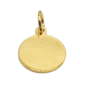 Pode incluir: Um amuleto redondo dourado com uma superfície lisa e um laço na parte superior para prender a um colar ou pulseira.