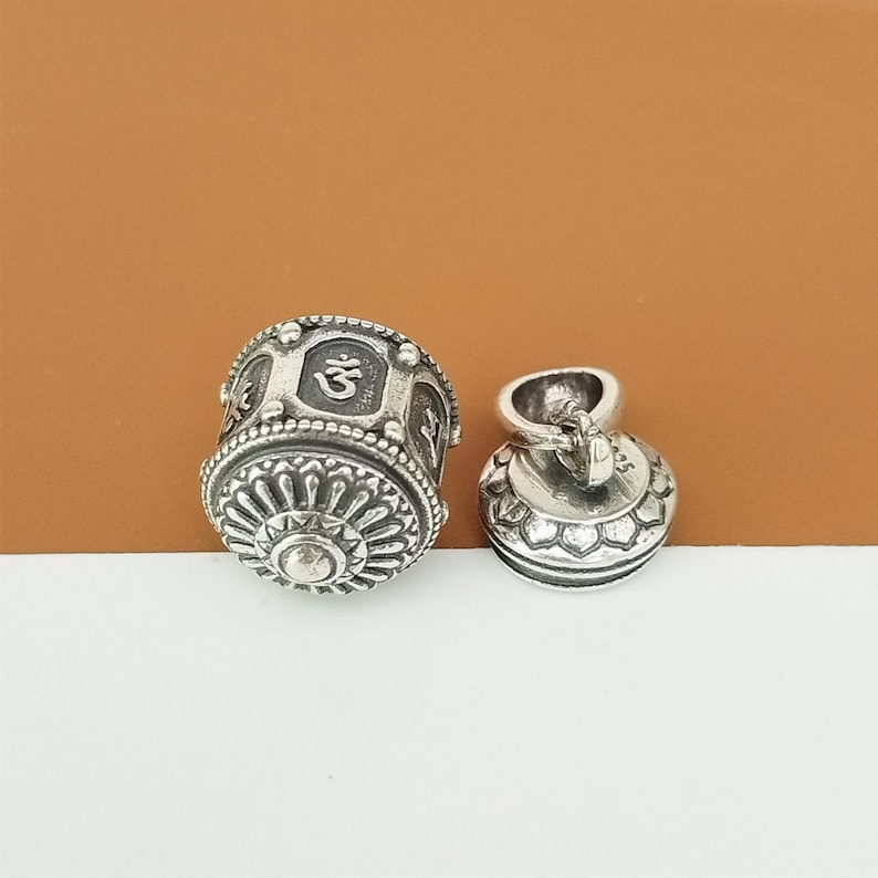 Puede incluir: P&eacute;ndulo de rueda de oraci&oacute;n de plata con un s&iacute;mbolo Om y detalles intrincados. El colgante est&aacute; unido a una cadena de plata.