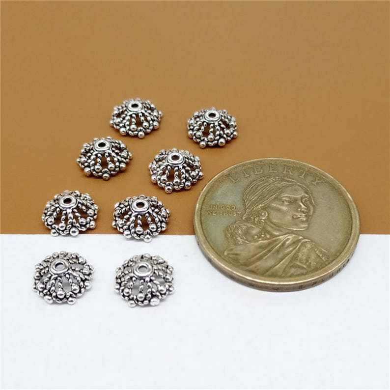 May include: Eight silver-toned metal bead caps with a decorative design. The bead caps are arranged in a circle around a US dollar coin.