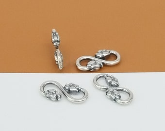 May include: Four silver infinity-shaped clasps with decorative floral details. The clasps are designed for jewelry making and are approximately 1 inch in length.