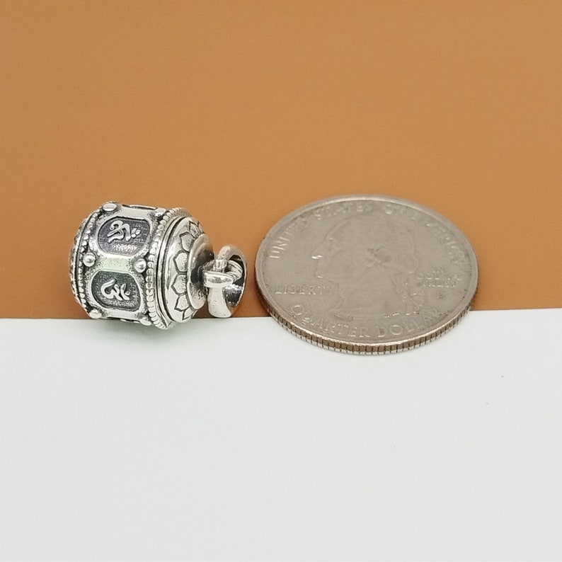 Puede incluir: Encanto de plata en forma de rueda de oraci&oacute;n con detalles intrincados y un bucle para sujetarlo a un collar o pulsera. El encanto se muestra junto a una moneda de 25 centavos de d&oacute;lar estadounidense para comparar el tama&ntilde;o.