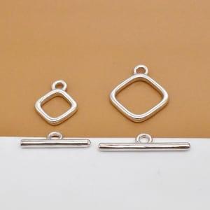 May include: Silver-toned jewelry findings, including two square toggle clasps and two diamond-shaped pendants. The clasps are horizontal bars with a loop, and the pendants have a loop at the top. The pieces are displayed against a neutral background.