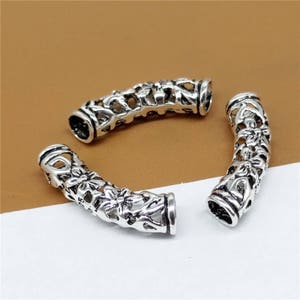 May include: Three silver-toned metal end caps with intricate floral designs. The end caps are hollow and have a rounded shape.