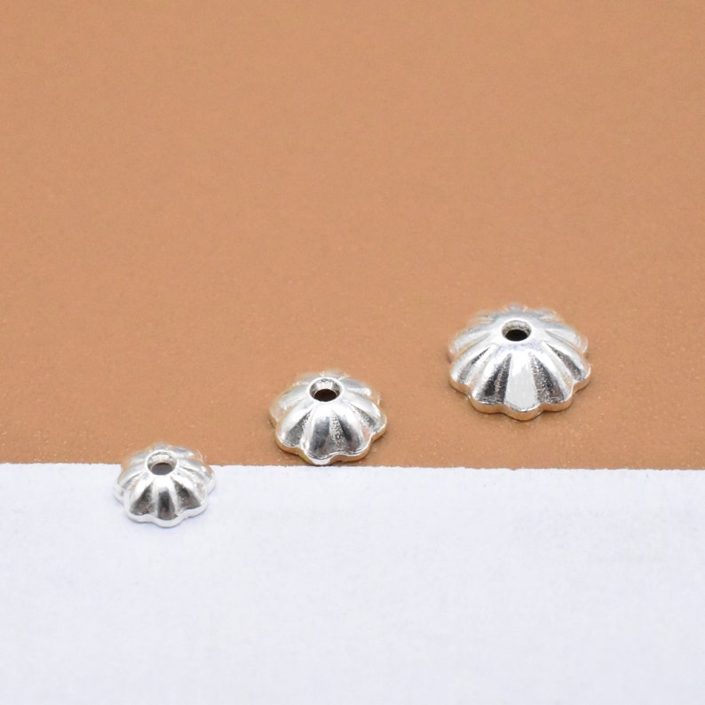 Op de afbeelding: Drie zilverkleurige metalen kralencaps in verschillende maten. De caps hebben een gegolfde rand en een klein gaatje in het midden.