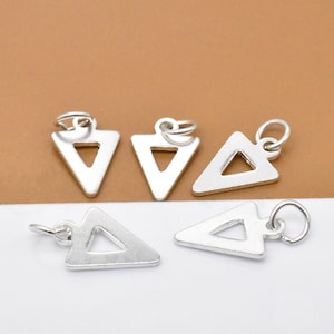 May include: Five silver triangle charms with a hole at the top for attaching to jewellery. The charms are hollow and have a simple geometric design.