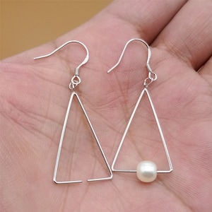 May include: A pair of silver triangle earrings with a single white pearl dangling from the bottom of one earring.
