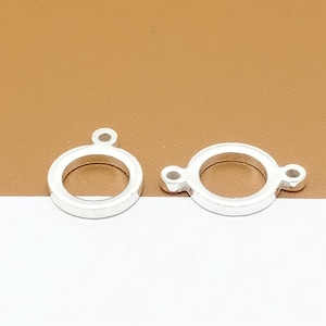 May include: Two silver-toned metal circle pendant charms with a small loop at the top and two small loops on the side.