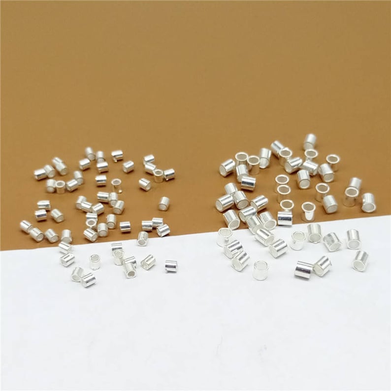 May include: A collection of silver-toned metal jump rings, ideal for jewelry making. The jump rings are arranged in two groups on a white surface.