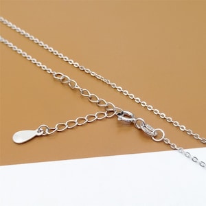 Op de afbeelding: Een zilveren ketting met een karabijn sluiting en een klein, traanvormig hangertje.