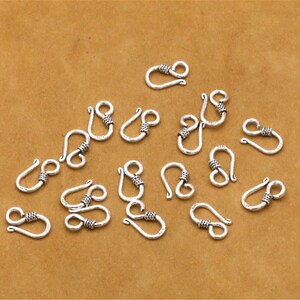 May include: A collection of 16 silver-toned lobster clasps with a twisted design. The clasps are arranged on a brown surface.