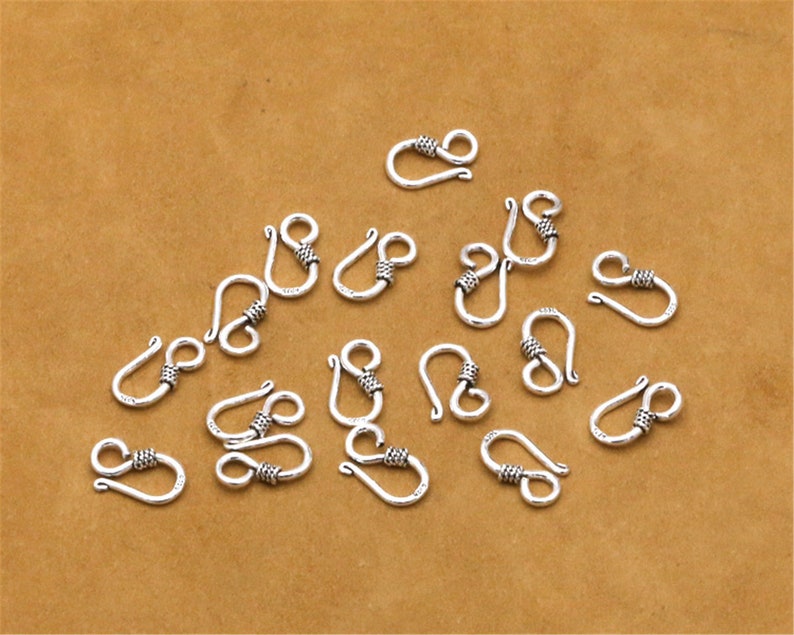 May include: A collection of 16 silver-toned lobster clasps with a twisted design. The clasps are arranged on a brown surface.