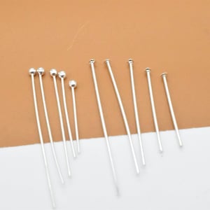 May include: A set of silver head pins with round heads. The pins are of varying lengths.