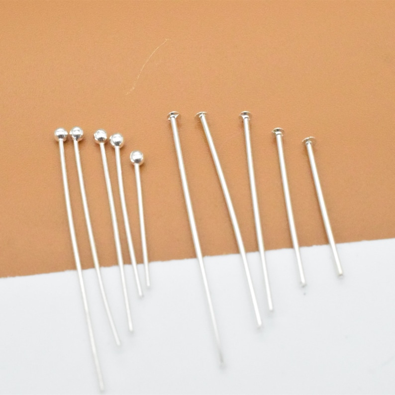 May include: A set of silver head pins with round heads. The pins are of varying lengths.