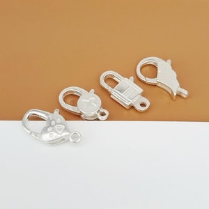 Könnte beinhalten: Vier silberfarbene Karabinerhaken mit unterschiedlichen Designs. Die Karabinerhaken befinden sich auf einer braunen Oberfläche.