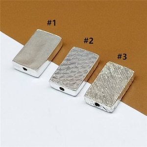 May include: Three silver rectangular metal beads with different textures. The first bead is smooth, the second bead has a textured pattern, and the third bead has a linear pattern. The beads are labeled #1, #2, and #3.