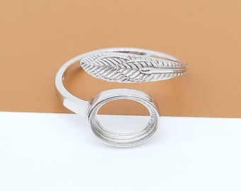 May include: A silver-colored ring with a feather design and a circular setting. The feather detail is textured, and the ring is adjustable. The ring is shown against a neutral background.
