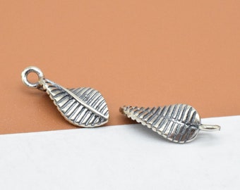 May include: Two silver leaf charms with a textured design. The charms have a loop at the top for attaching to jewelry.
