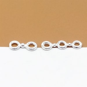 May include: Two silver jump rings, one with two loops and one with three loops. The rings are smooth and shiny.